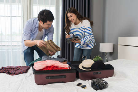 couple check a list of things with a tablet, prepare and packing clothes into suitcase on a bed, planning travel holiday.の写真素材