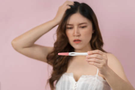 stessed pregnant woman holding and showing the positive pregnancy test on pink backgroundの写真素材