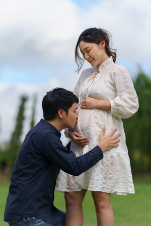 married couple is expecting a baby. man kissing belly of his pregnant wife in the parkの写真素材
