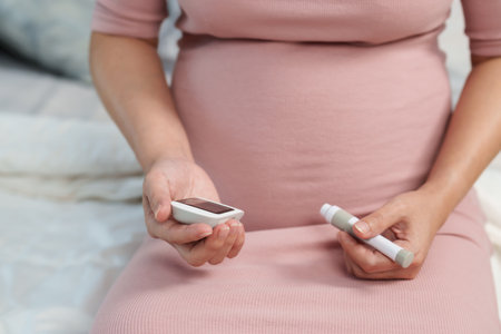 close up of pregnant woman holding glucose meter and checking blood sugar level by herself at home. gestational diabetes concept.の写真素材