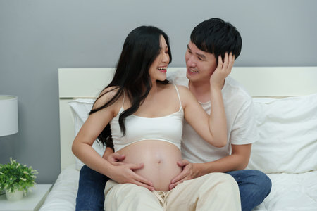 married couple is expecting baby. man embraces his pregnant wife on a bedの写真素材