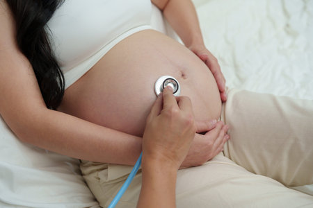 close up pregnant couple listening to baby heartbeat in her belly with a stethoscope on a bed