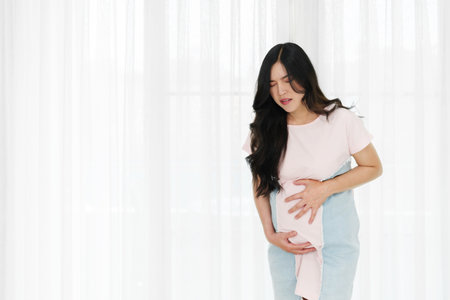 pregnant woman has a stomachache on window backgroundの写真素材
