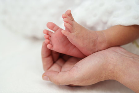 mother hand holding newborn baby feet on a bed
