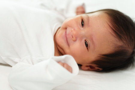 happy newborn baby smilling while lying on a white bed
