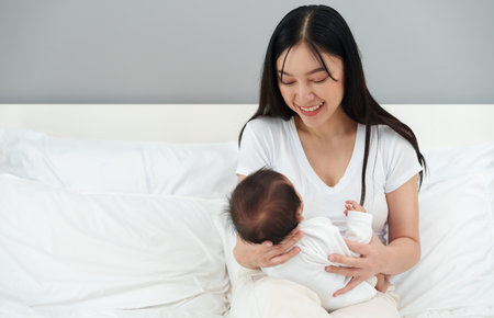 happy mother holding and playing with her newborn baby on a bedの写真素材