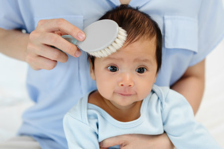 mother combing her newborn baby hair on a bedの写真素材