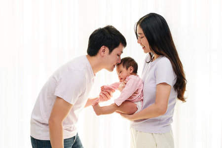 father kissing newborn baby while mother holding her on white window background. happy family conceptの写真素材