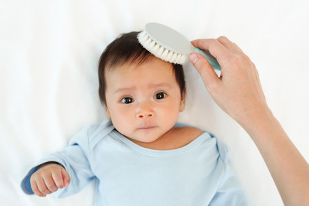 mother combing her newborn baby hair on a bedの写真素材