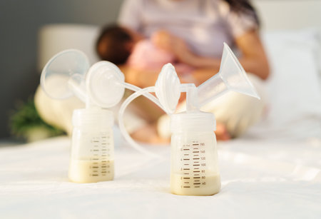 the breast milk are in the bottles of electric breast pumping set on a bed with mother breastfeeding newborm baby backgroundの写真素材