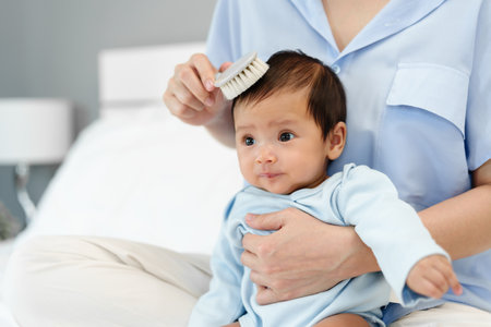 mother combing her newborn baby hair on a bedの写真素材