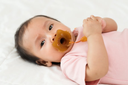 infant baby girl suck with pacifier on a bedの写真素材