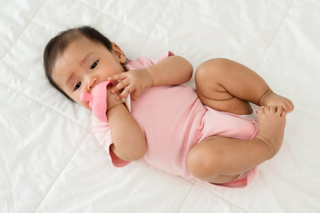 infant baby biting mushroom teether rubber toy on a bedの写真素材