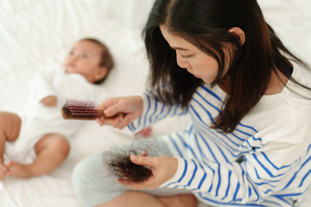 stressed mother having hair loss postpartum problem with her baby at homeの写真素材