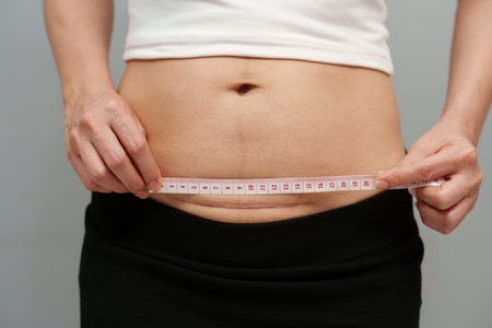 woman using tape measuring the c-section scar of cesarean on her bellyの写真素材