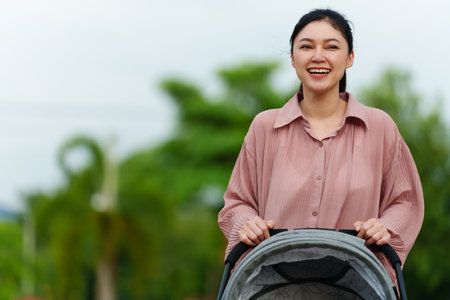 happy mother pushing infant baby stroller and walking in the parkの写真素材