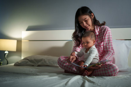 mother read story in the book for infant baby on a bed at nightの写真素材
