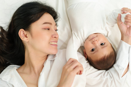 happy mother lying and playing with her infant baby on a bed (top view)の写真素材