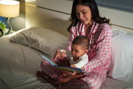mother read story in the book for infant baby on a bed at nightの写真素材