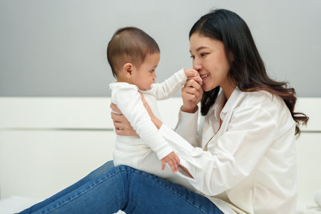 mother kissing hand of her infant baby on a bedの写真素材
