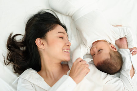 happy mother lying and playing with her infant baby on a bed (top view)の写真素材