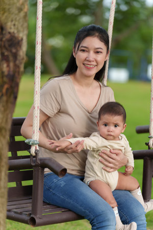 mother with her baby sitting on a swing in the parkの写真素材