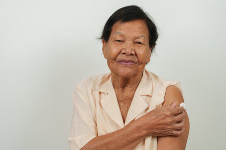 older happy senior woman showing cotton on arm after getting a vaccineの写真素材