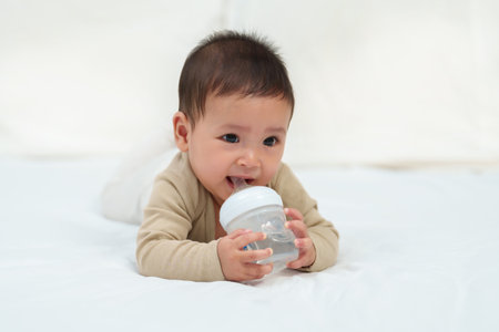 baby drinking water from bottle on a bed