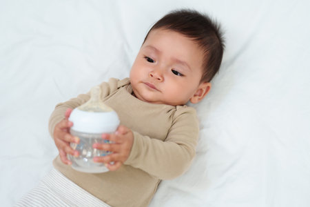baby drinking water from bottle on a bedの写真素材