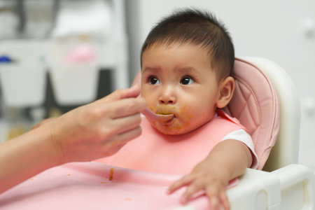 mother feeding food to her infant baby eating with a spoon at homeの写真素材