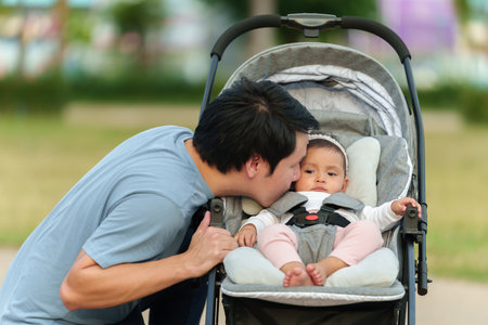 father kissing with his infant baby in the stroller while resting in the parkの写真素材