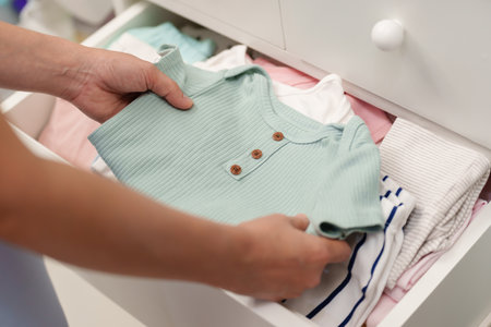 hand of mother taking baby clothes from open cabinet drawerの写真素材