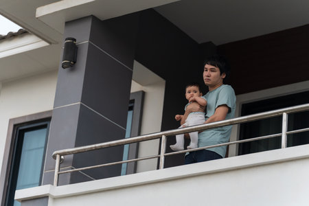 stressed father and infant baby at balcony of their houseの写真素材