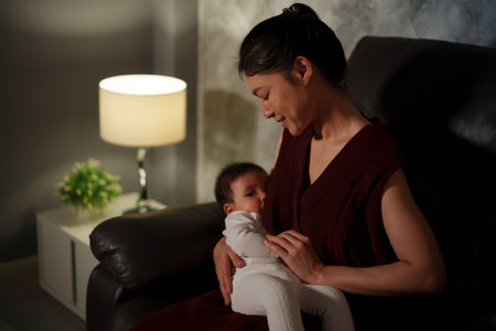 mother breastfeeding infant baby on a sofa in the living room at nightの写真素材