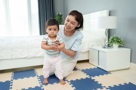 infant baby learning to standing with mother on a mat floor in the bedroom