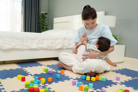 mother breastfeeding infant baby after playing wooden block in the bedroomの写真素材