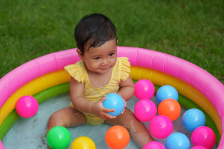 happy infant baby girl playing water with colorful plastic balls in the inflatable poolの写真素材