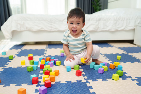 happy infant baby playing wooden block toy on jigsaw mat in the bedroomの写真素材