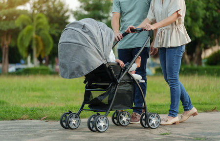 parent (father and mother) pushing infant baby stroller and walking in the park