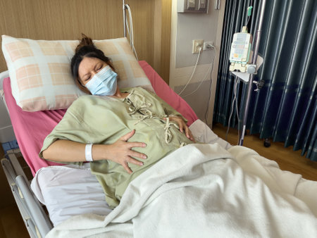 pregnant woman patient wearing medical mask while has a stomachache on a bed in hospitalの写真素材