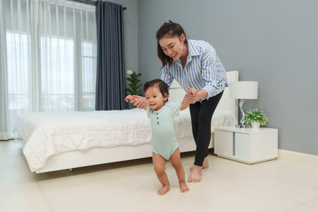 infant baby learn walking first step with mother holding hand helping at homeの写真素材
