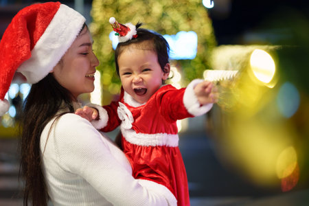 cheerful mother with her daughter in santa dress and christmas light at night. happy new year eveの写真素材