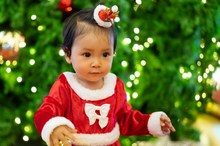 happy toddler girl in santa dress and christmas tree background. happy new year eveの写真素材
