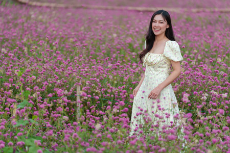 beautiful woman in a dress enjoying blooming pink globe amaranth or bachelor button flower fieldの写真素材