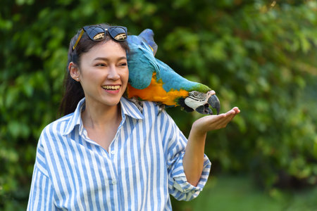happy woman feeding blue-and-yellow macaw (Ara ararauna) bird on her handの写真素材