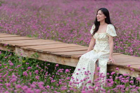 beautiful woman in a dress enjoying blooming pink globe amaranth or bachelor button flower fieldの写真素材