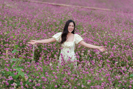beautiful woman in a dress enjoying blooming pink globe amaranth or bachelor button flower fieldの写真素材
