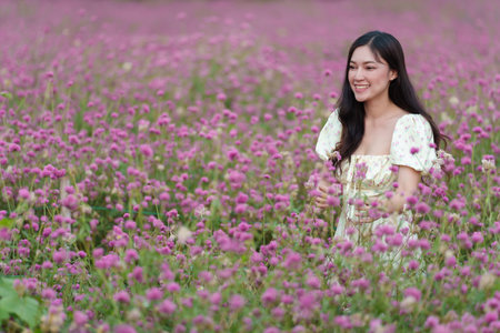 beautiful woman in a dress enjoying blooming pink globe amaranth or bachelor button flower fieldの写真素材