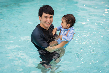 happy father holding baby in his arms while playing in a swimming poolの写真素材