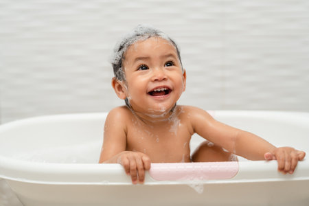 happy infant baby take a bath and playing with foam bubbles in bathtub at homeの写真素材